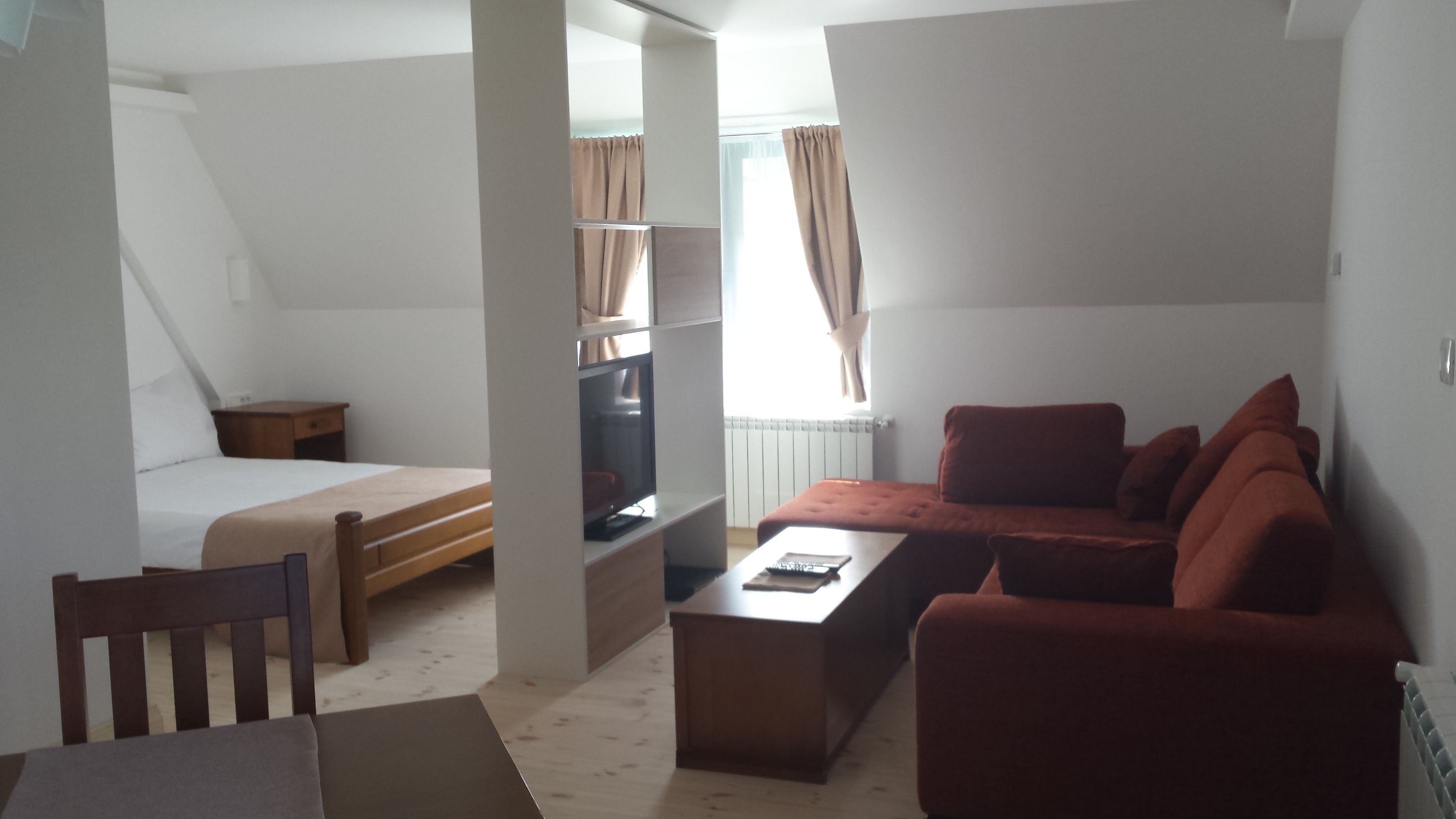 Quarto compacto com uma cama, um sofá, uma TV e uma pequena mesa.