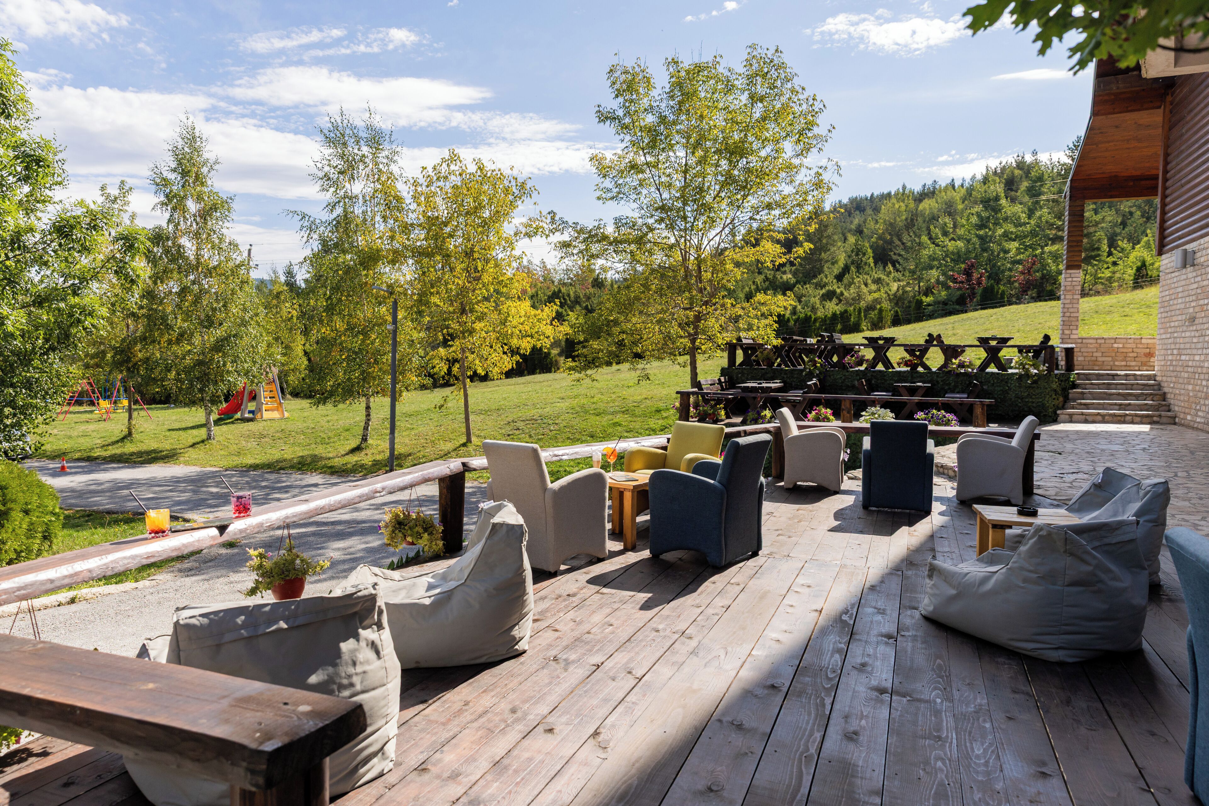 A wooden deck with outdoor seating, a picnic table, and a view of a green landscape with trees and a hill.