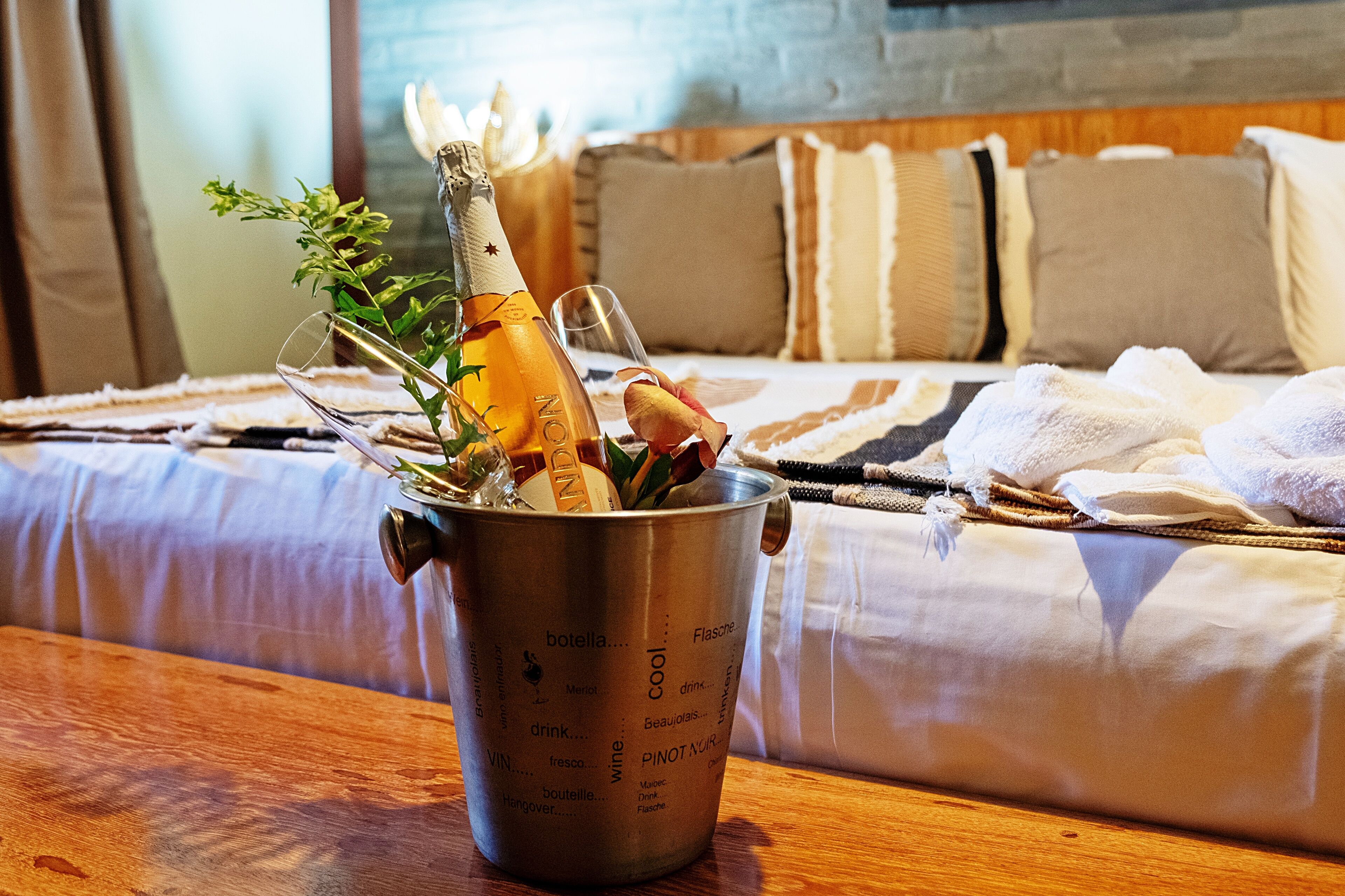 Une bouteille de champagne dans un seau à glace, avec des verres et une rose, sur une table en bois dans une chambre d’hôtel.