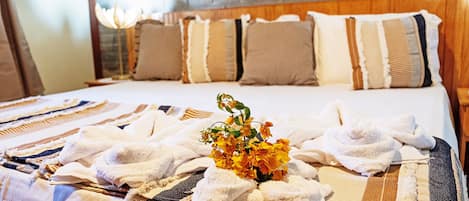 A hotel room with a bed, pillows, a blanket, and a vase with flowers.