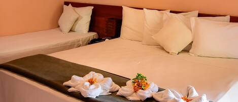 A hotel room with two single beds, a large bed, a painting of sunflowers, a ceiling light, and a wall-mounted air conditioner.