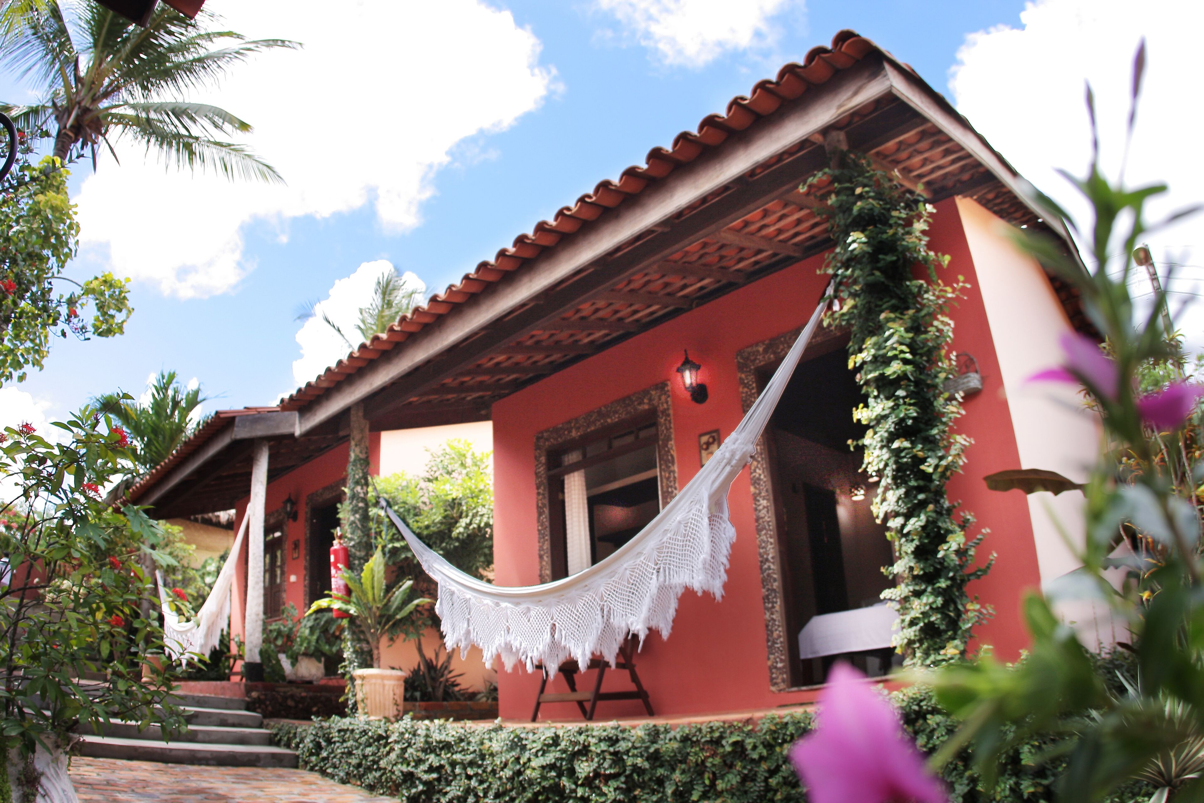 A red building with a hammock, steps, and a garden.