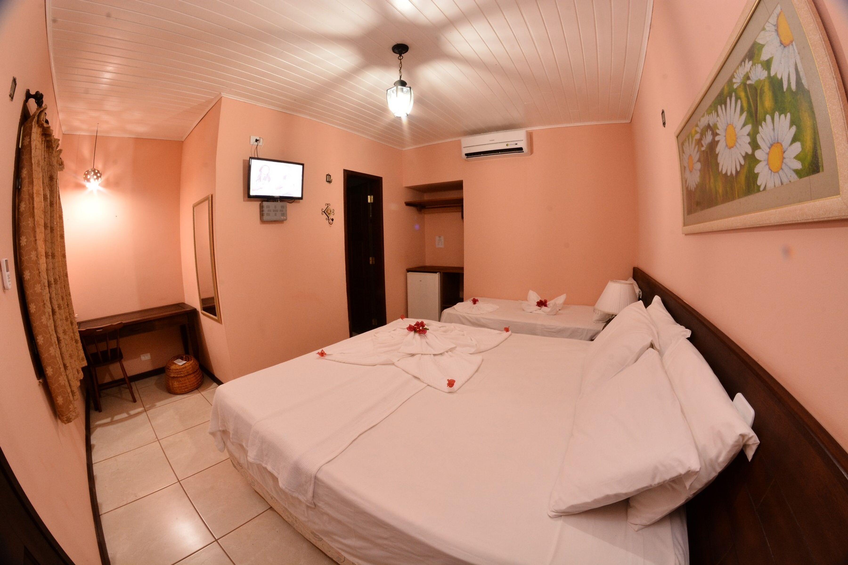 A hotel room with a bed, a desk, a chair, a television, and a painting on the wall.