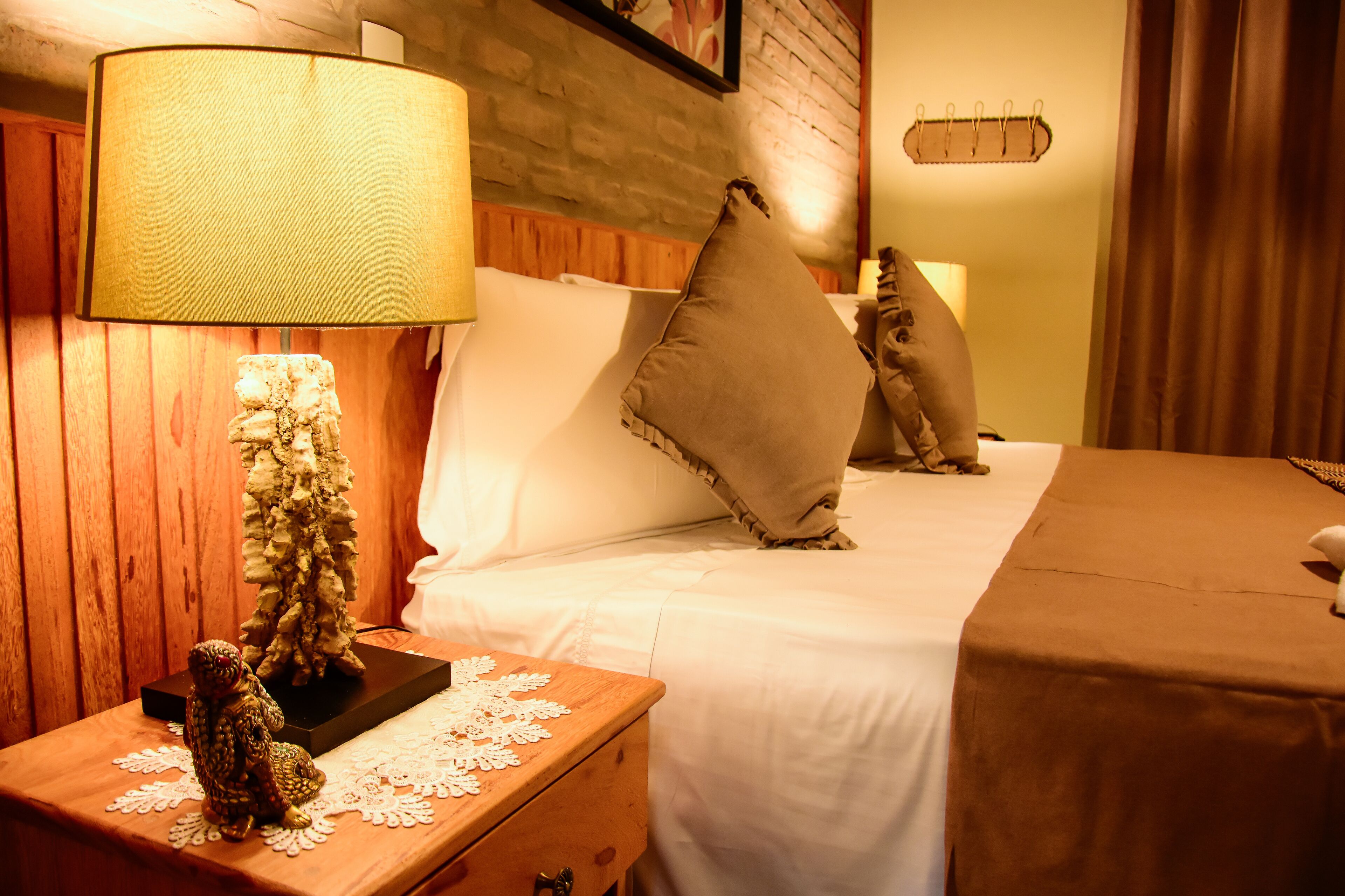 A neatly made bed with white linens, a wooden nightstand with a lamp, and a small decorative tree.