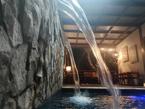 A stone wall with a water feature, a pool, and a dining area with tables and chairs. - Encantes do Nordeste (Barreirinhas)