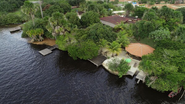 An aerial view of a riverside property with a wooden dock, a small pavilion, and lush greenery. - Encantes do Nordeste (Barreirinhas)