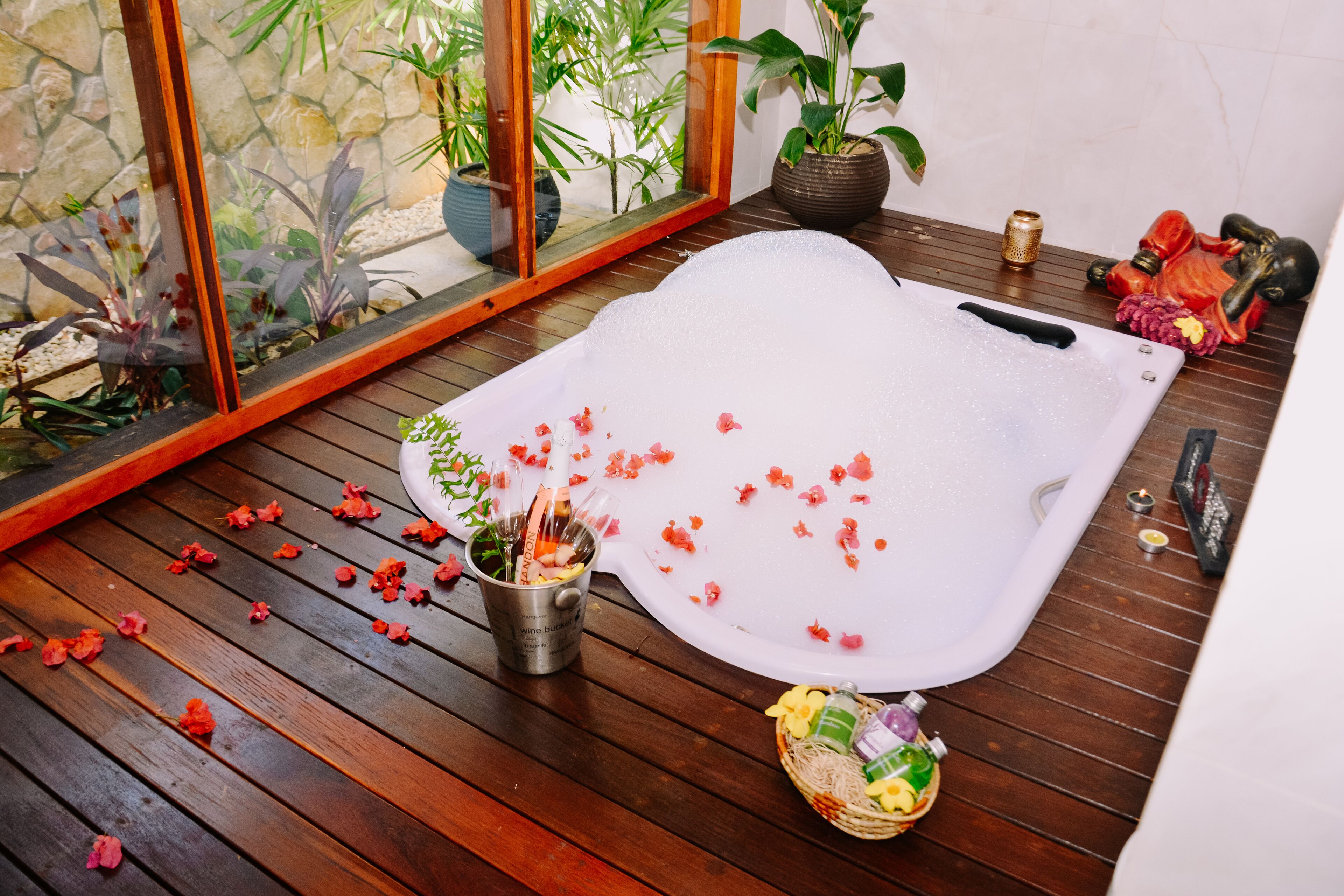 A spa area with a large white bathtub, wooden flooring, potted plants, and a small Buddha statue.