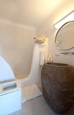 A modern bathroom with a bathtub, a large stone sink, and a mirror.