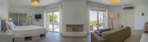 A modern bedroom with a bed, a television, a fireplace, and a balcony with a wicker sofa.