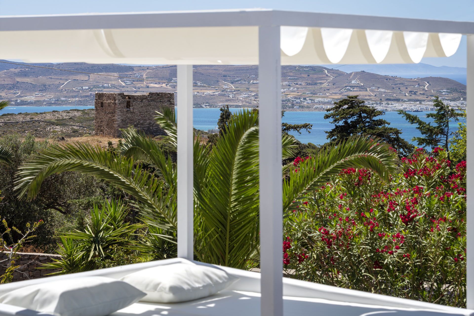 Ein Zimmer mit Bett, weißem Baldachin und Blick auf eine Küstenlandschaft mit Burg, Grünflächen und einem Gewässer.