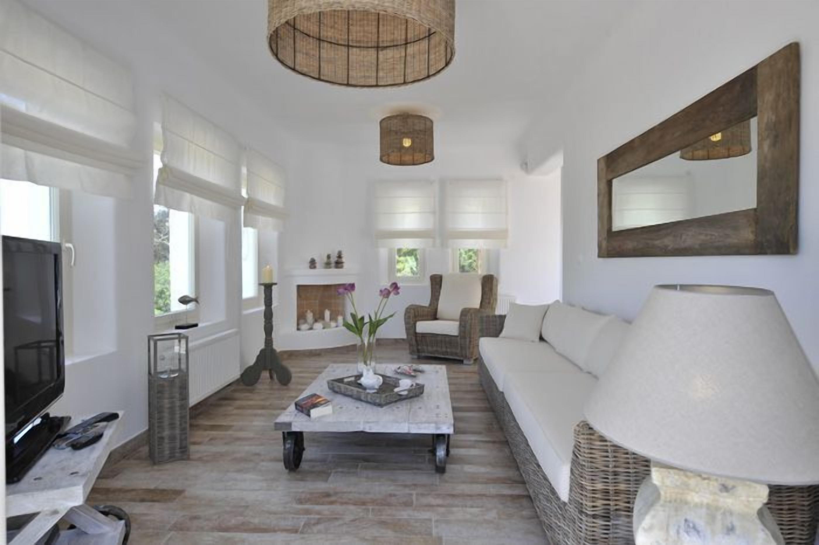 Uma sala de estar ampla com uma televisão grande, uma mesa de centro com objetos decorativos, um sofá e um abajur.