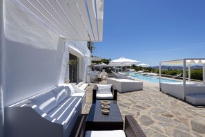 A poolside area with white furniture, a stone floor, and umbrellas.