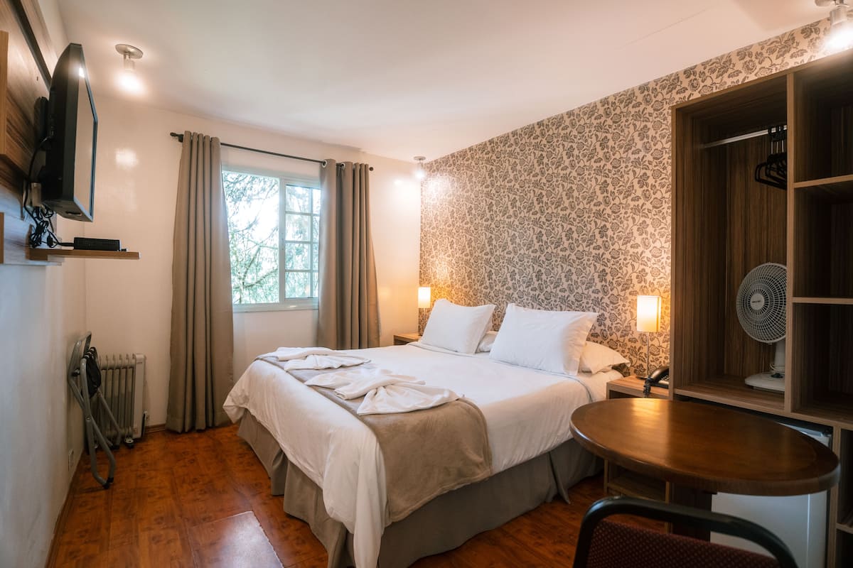 Hotellihuone, jossa on sänky, yöpöytä ja pieni pöytä tuolilla.