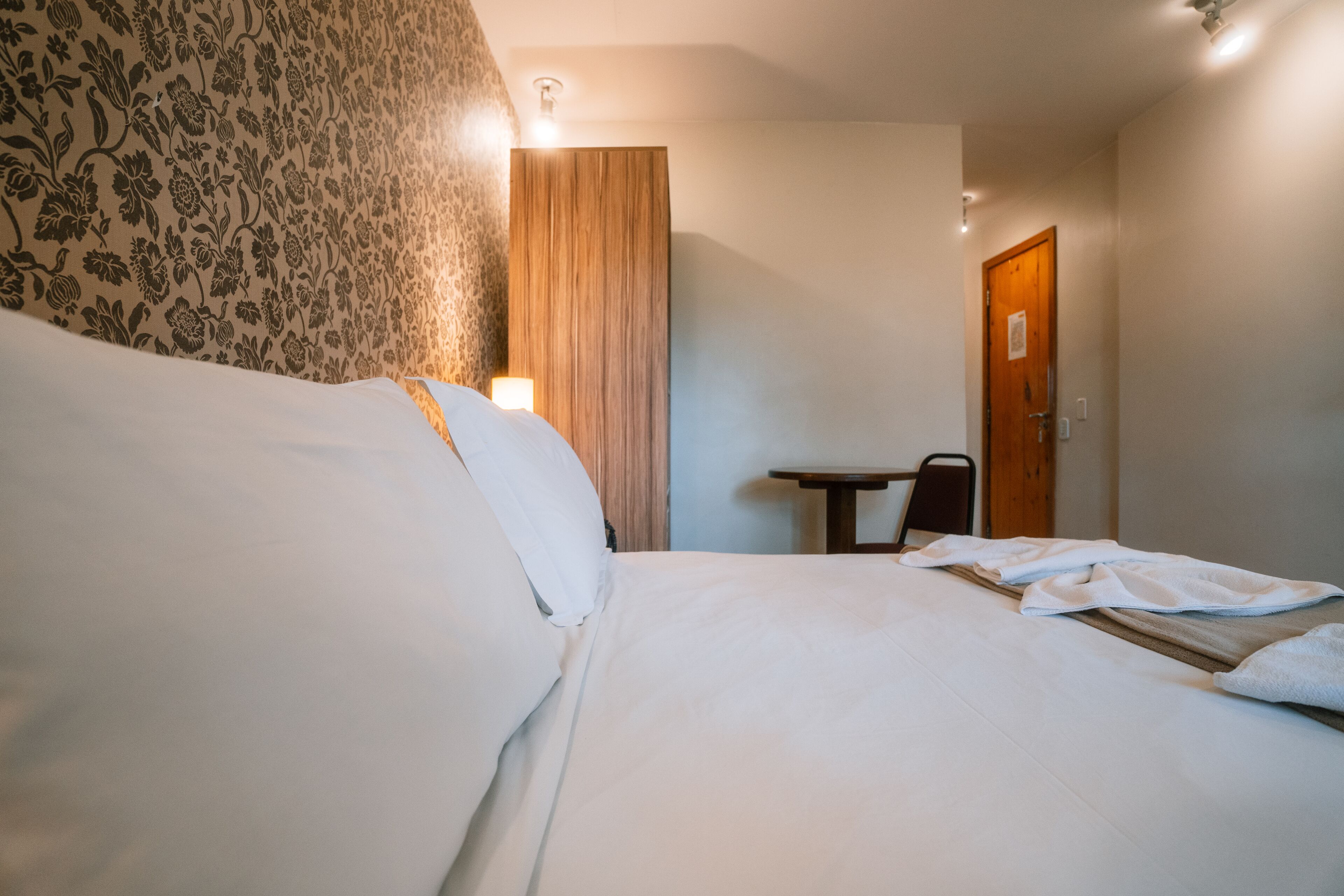Une chambre d’hôtel avec un grand lit, une tête de lit en bois, une petite table et une porte.