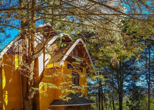 A yellow wooden cabin with a sign reading "Pawsada La Toza." - Pousada La Toscana (Campos do Jordão)