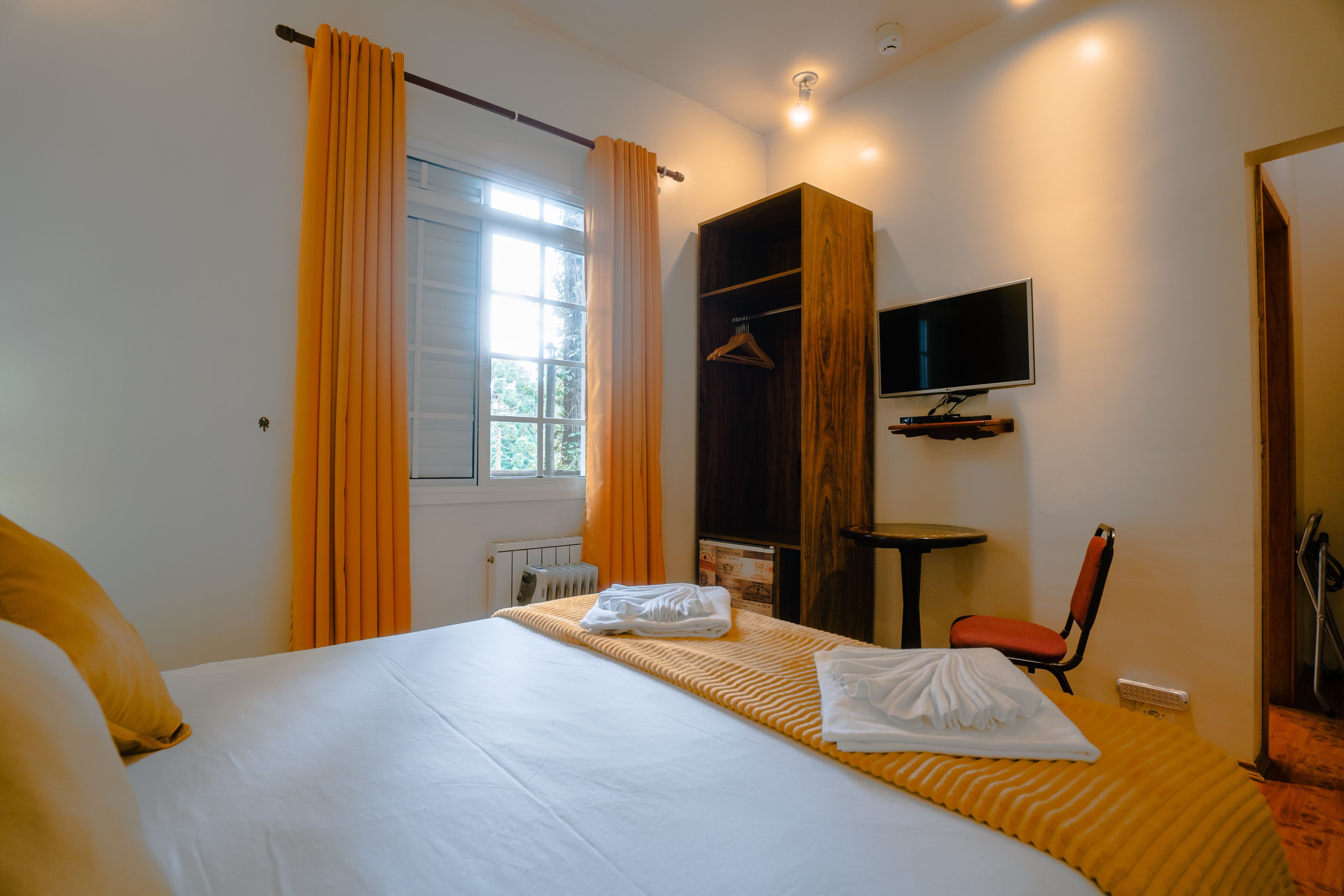 Une chambre d’hôtel avec un lit, un téléviseur fixé au mur, une chaise et une armoire en bois.
