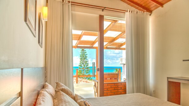 A bedroom with a large bed, a view of the sea, and a balcony with a wooden railing. - Pousada Ilha da Saudade (Cairu)