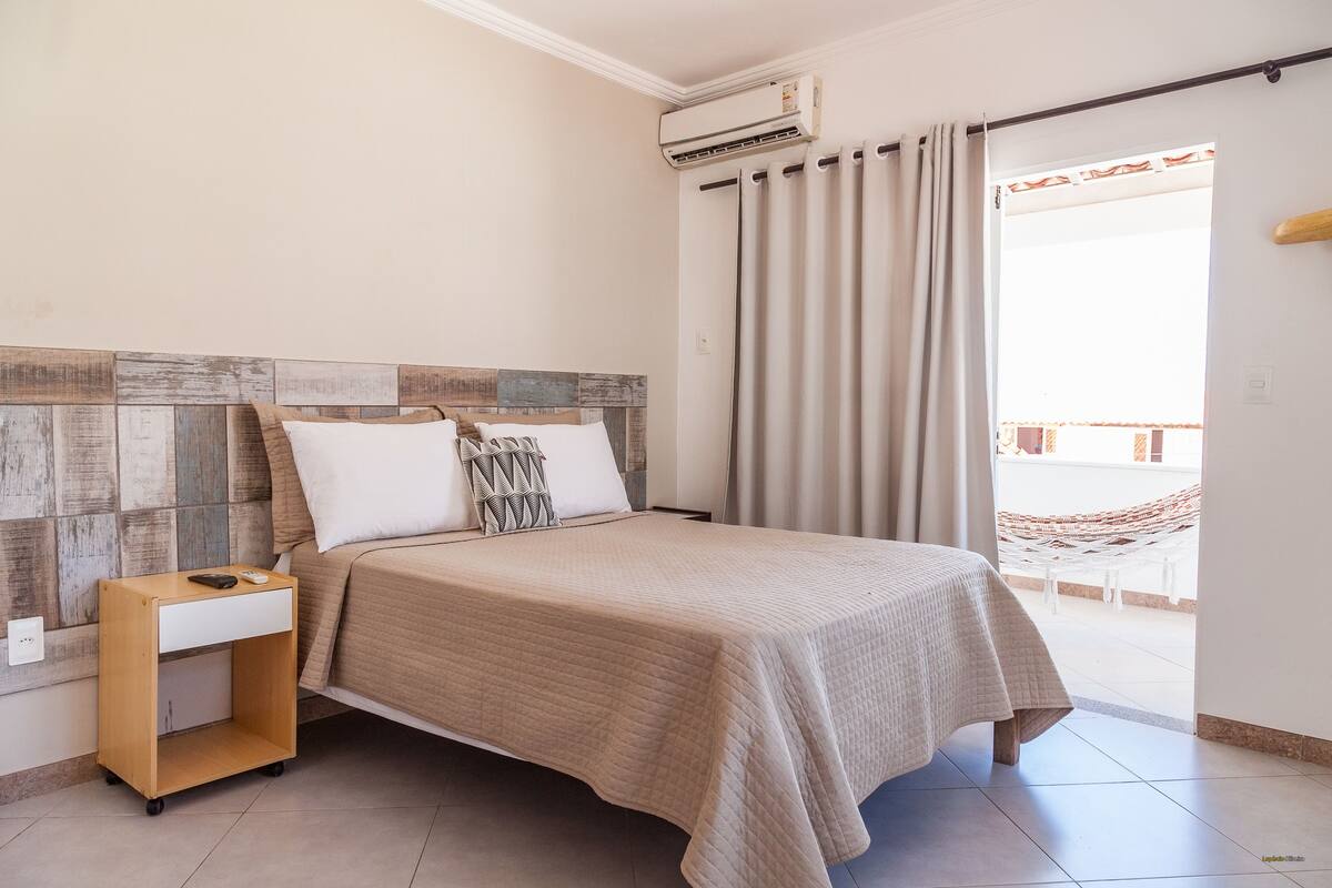 Un dormitorio con cama, mesita de noche, aire acondicionado de pared y vistas a un espacio exterior.