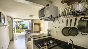 A compact kitchen with a microwave, stove, sink, and hanging pots. - Pousada Ilha da Saudade (Cairu)