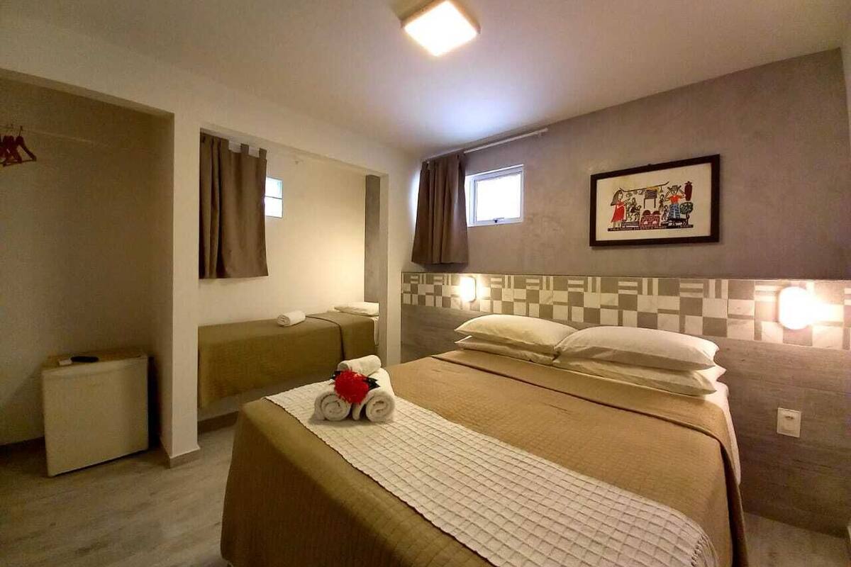 Una habitación de hotel con cama, mesita de noche, un escritorio pequeño, una silla, una ventana y una obra de arte colgada en la pared.