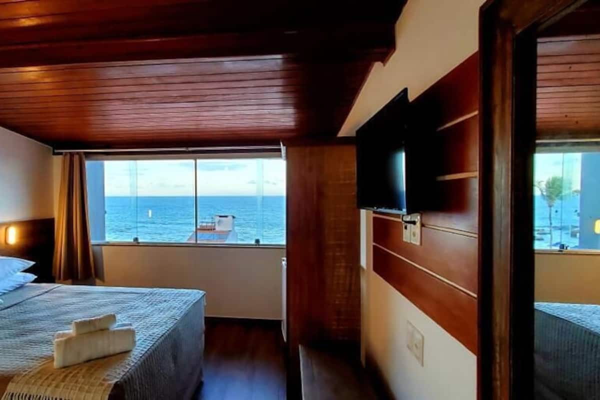 Habitación de hotel con una cama, una ventana que da al mar y techo de madera.