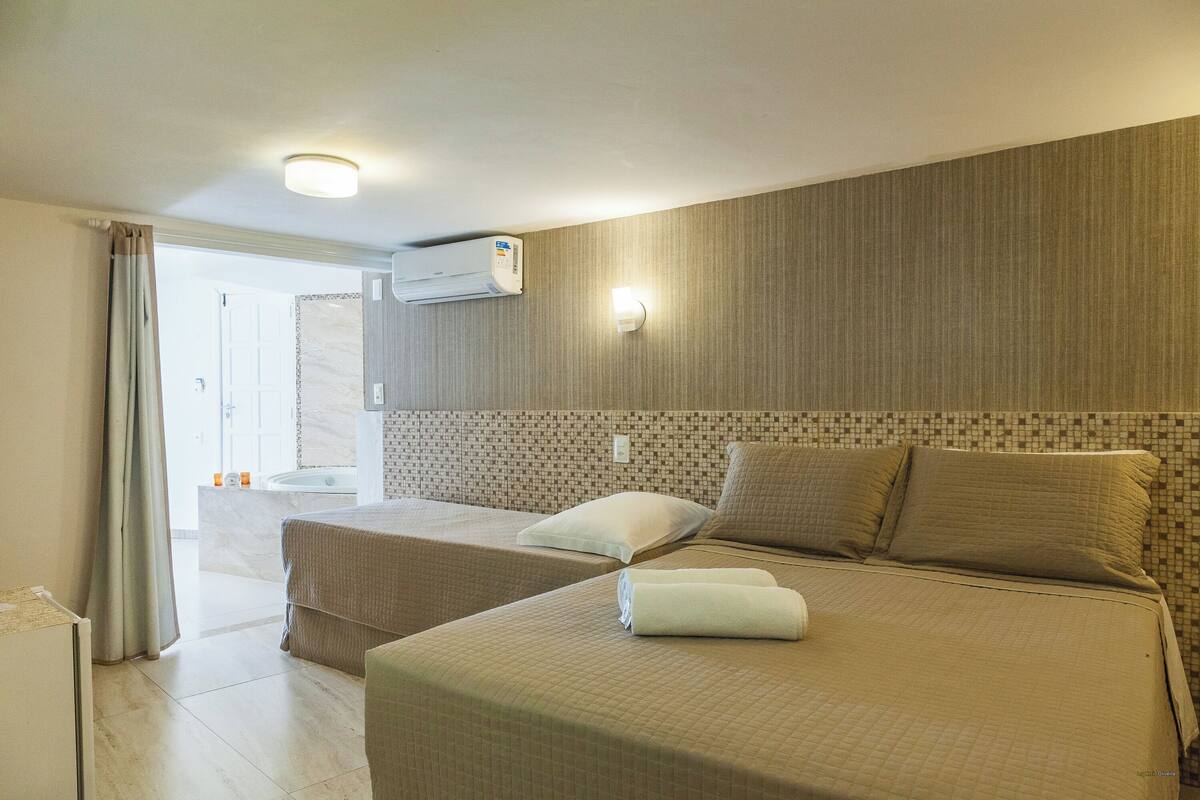 Habitación de hotel con dos camas, baño con bañera y aire acondicionado instalado en el techo.