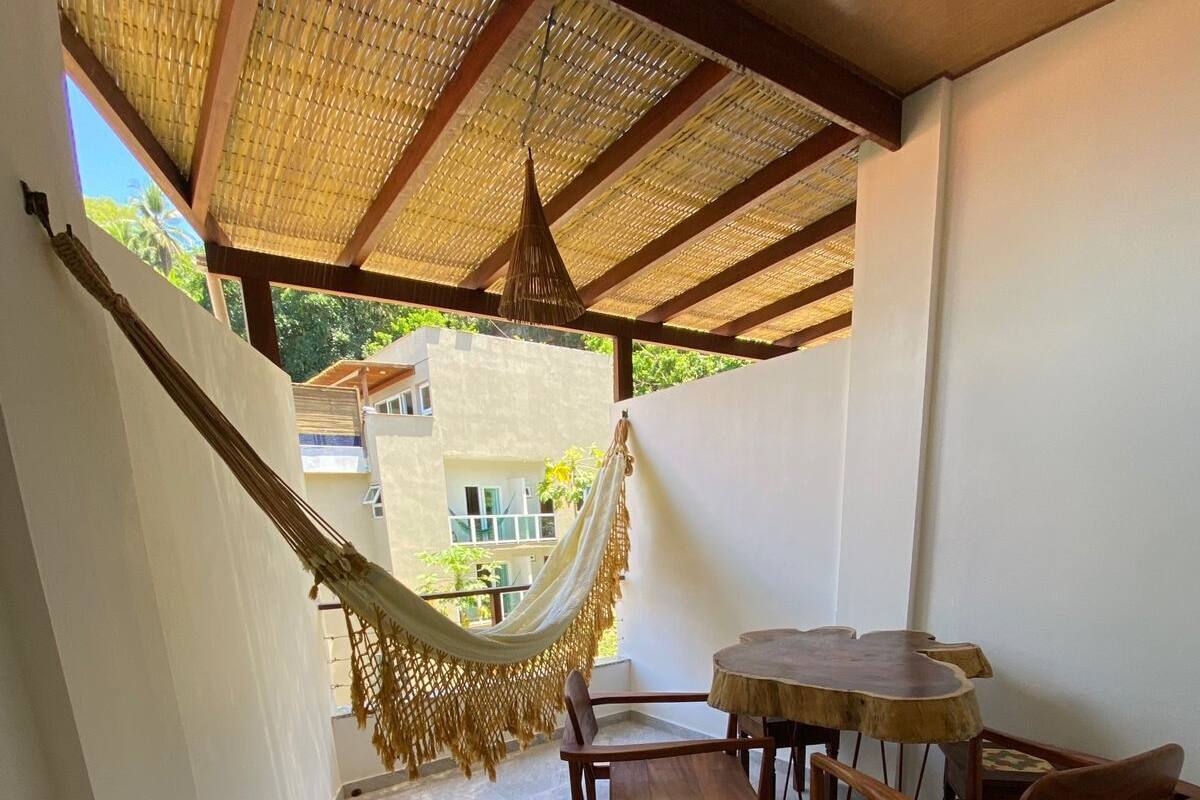 Un patio techado con una hamaca, sillas de madera y una mesa redonda.