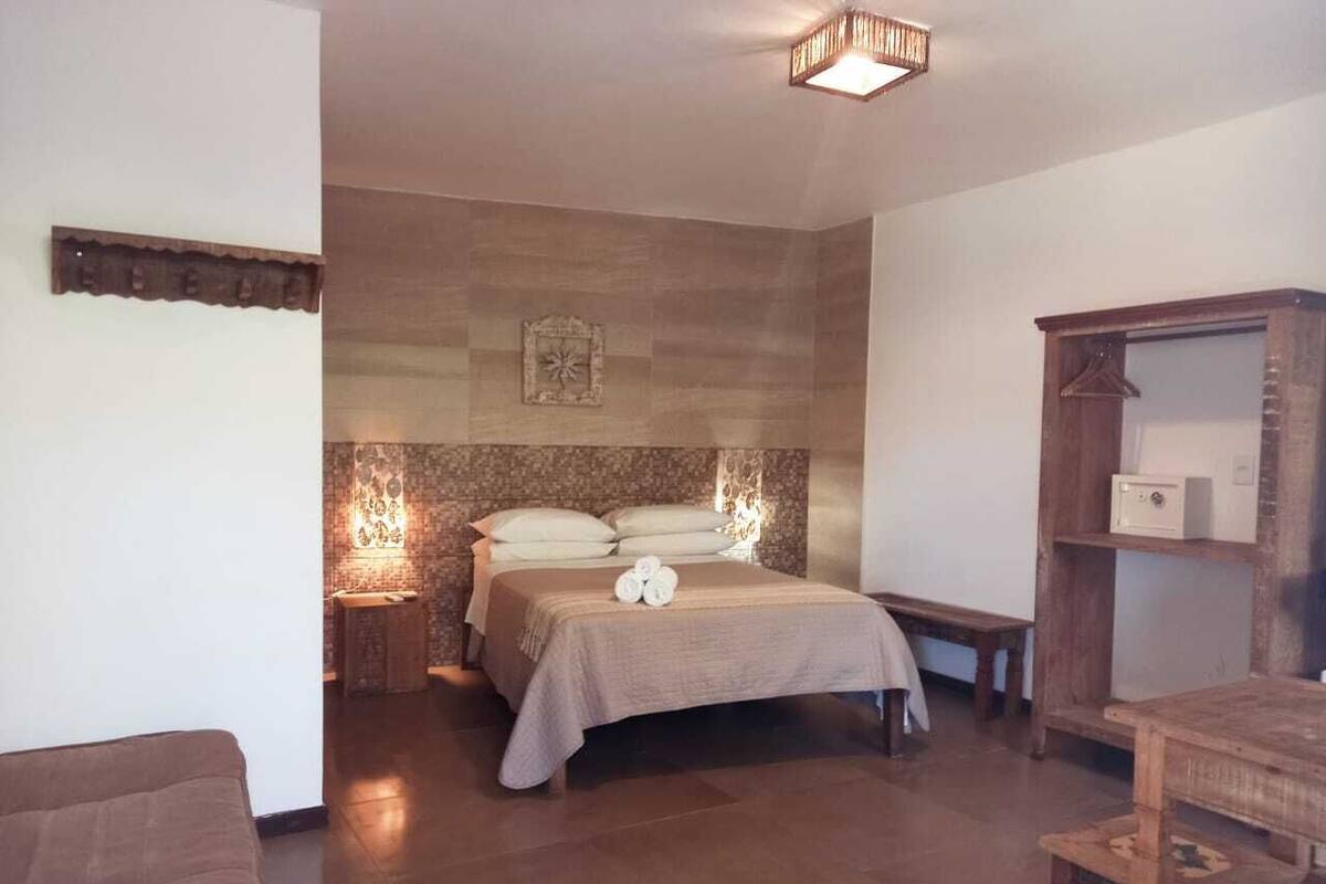 Un dormitorio con cama, mesitas de noche, un banco de madera y un armario.