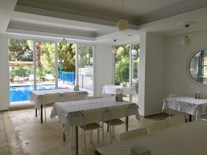 A dining area with tables and chairs, large windows with a view of a swimming pool and greenery. - Status Hotel (Fethiye)