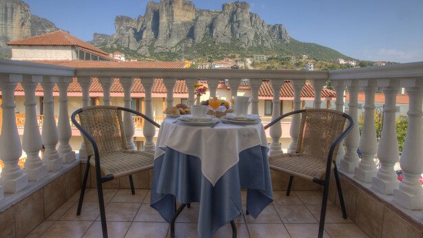A balcony with a table set for two, overlooking a mountainous landscape. - Hotel Kaikis (Kalabaka)