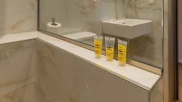 Un bany modern amb un separador de vidre, una paret de marbre, un lavabo i articles de tocador a la superfície.