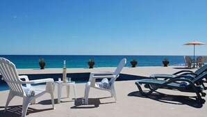 En avslappnad lounge vid stranden med solstolar och ett litet bord, med utsikt över havet.