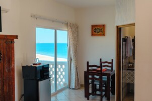 A room with a view of the sea, a wooden chair, a small table, and a refrigerator.