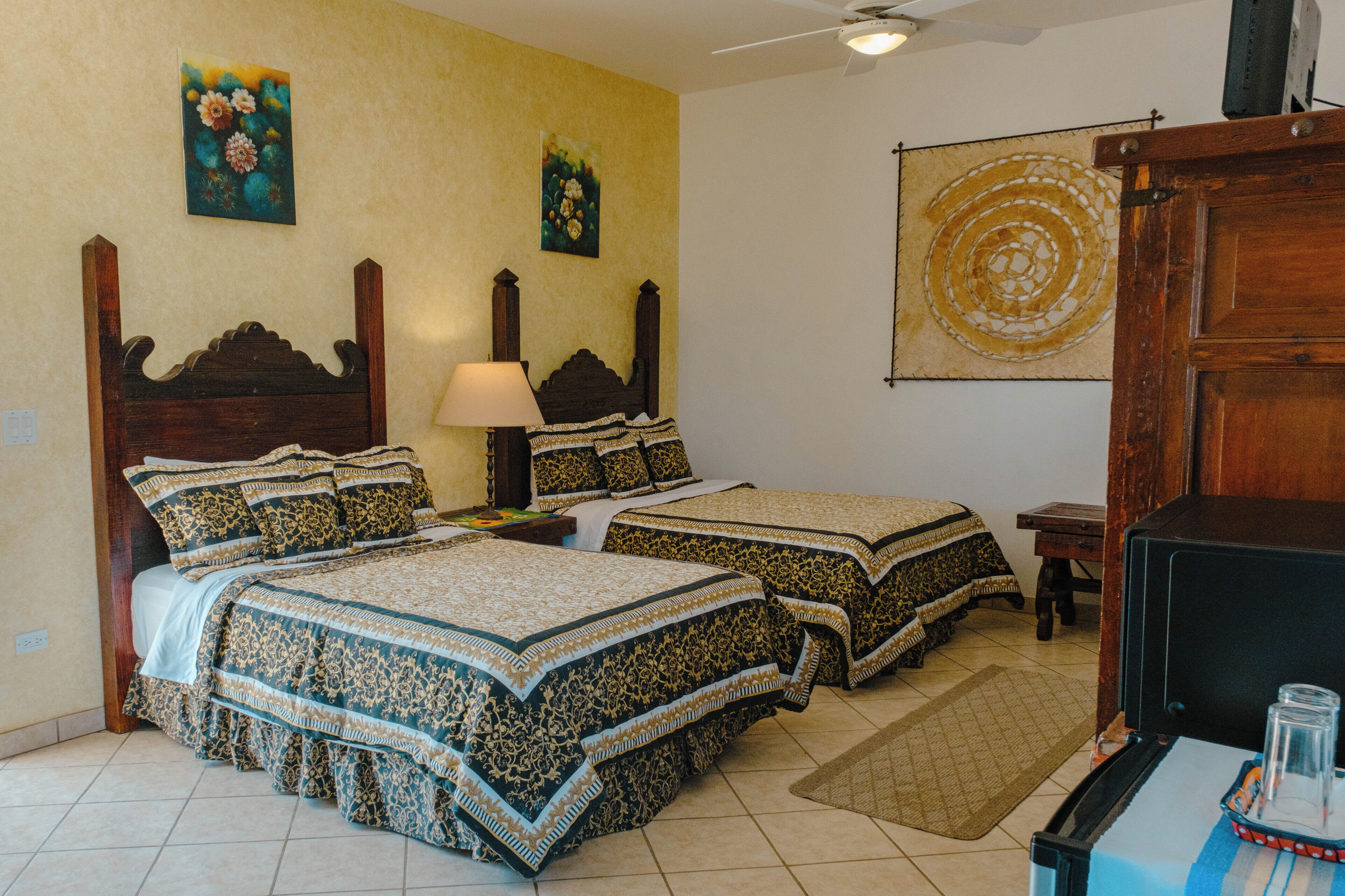A room with two beds, a nightstand, a lamp, a wooden cabinet, and a wall with a circular design.