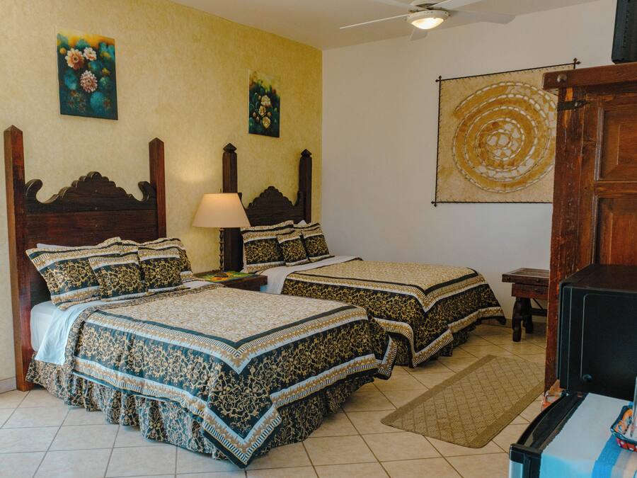 A room with two beds, a nightstand, a lamp, a wooden cabinet, and a wall with a circular design.