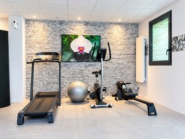 Un gimnasio en casa con cinta de correr, bicicleta estática, elíptica y una pelota de ejercicios grande.