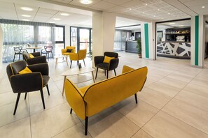 A modern hotel lobby with yellow and black seating, a reception area, and a bar.
