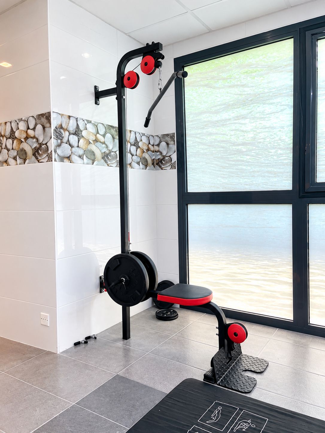 A gym with a weightlifting station, a bench, and a window with a view of water.