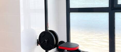 A gym with a weightlifting station, a bench, and a window with a view of water.
