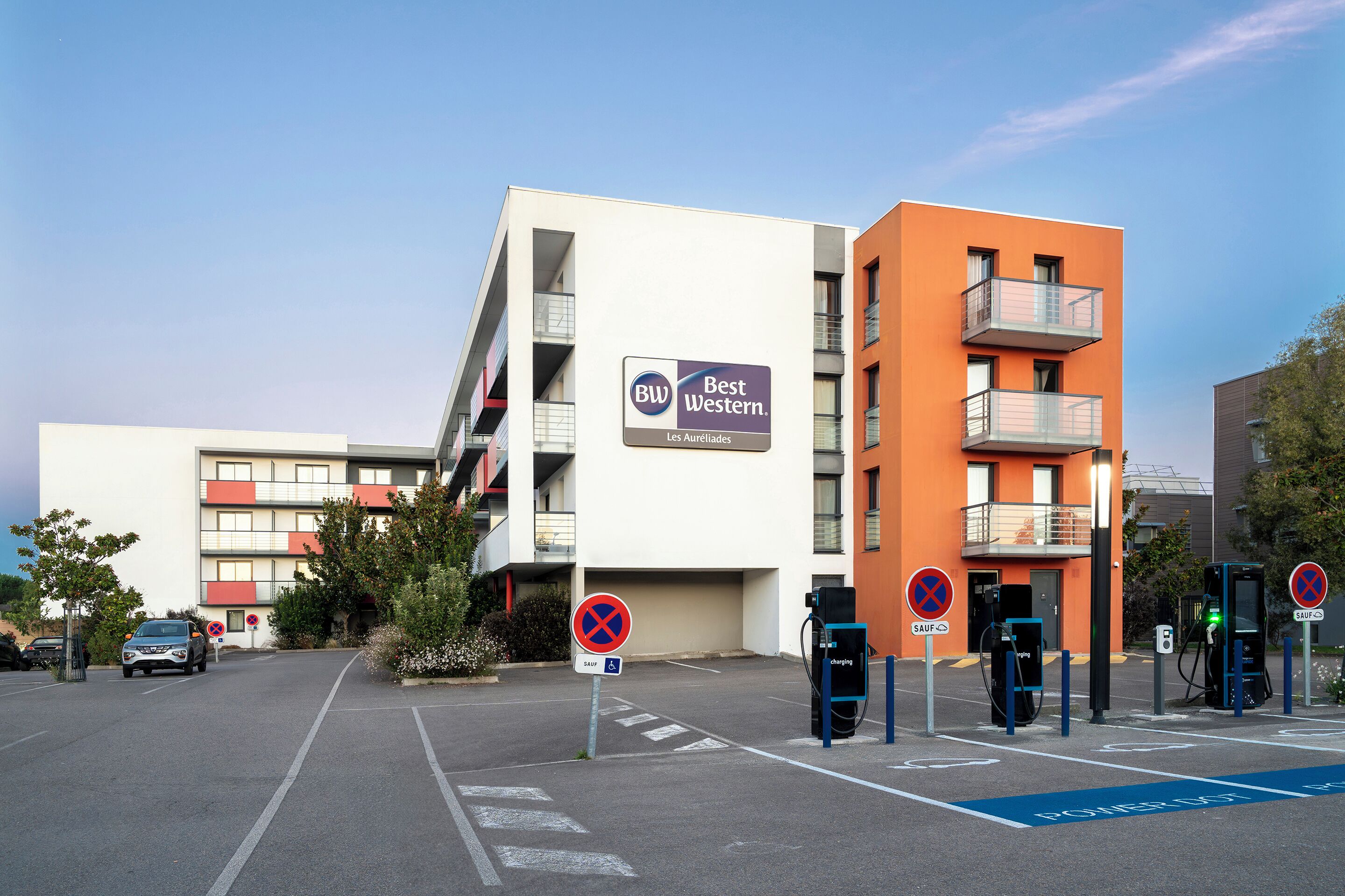 A modern building with a sign reading "Best Western." There are electric vehicle charging stations and a parking area with marked spaces.