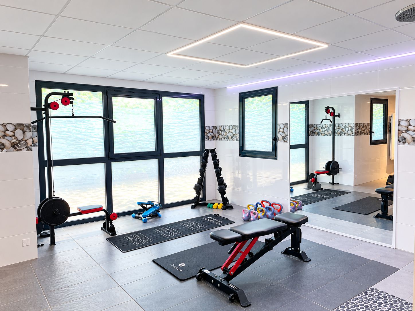 Un gimnasio con equipo de ejercicio, ventanas amplias y un espejo.