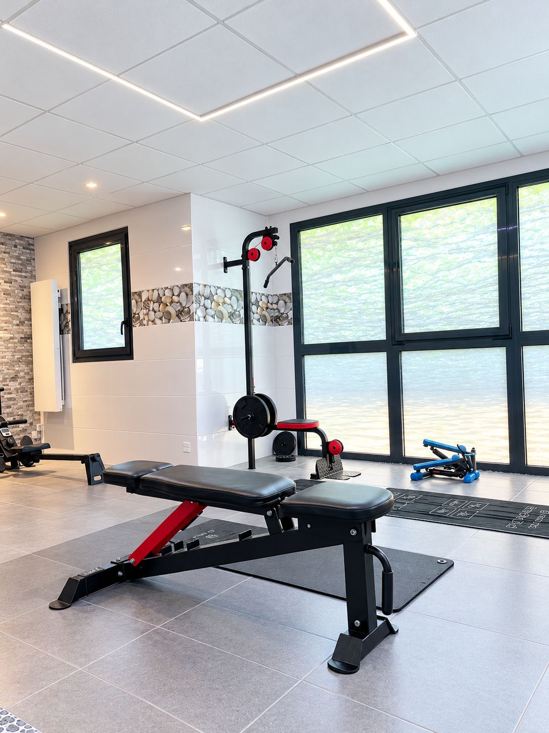Ein Fitnessraum mit einer Hantelbank, einem Squat-Stand und einem Rudergerät.