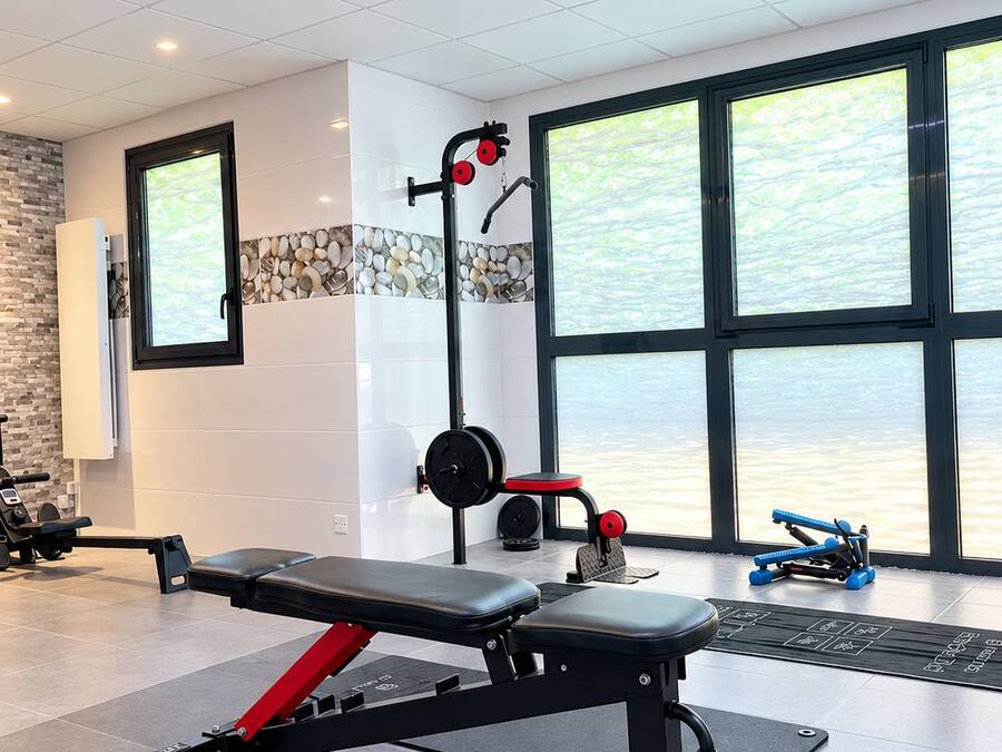 Ein Fitnessraum mit einer Hantelbank, einem Squat-Stand und einem Rudergerät.