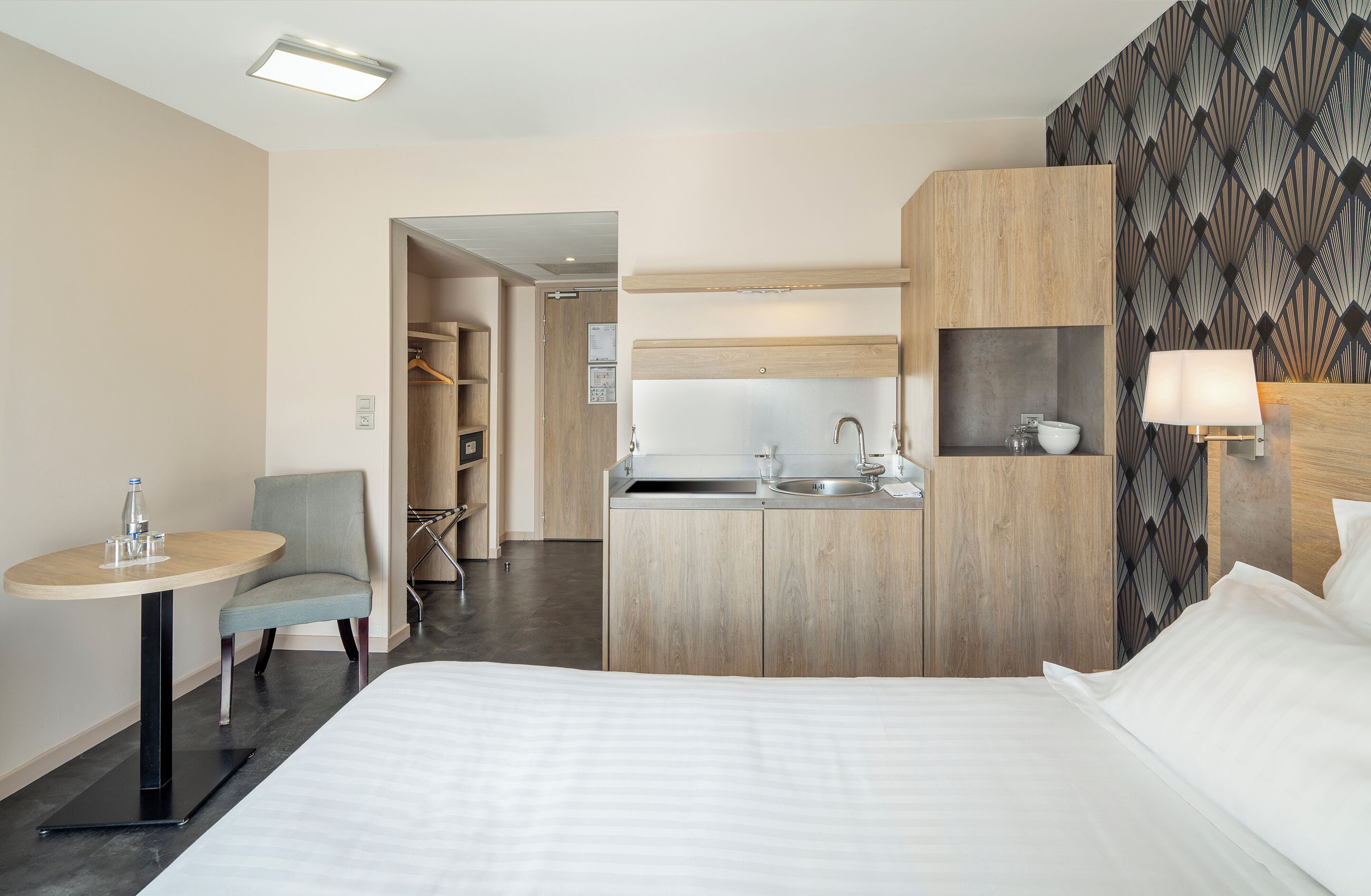 Una habitación de hotel con cama, una pequeña mesa con silla, kitchenette y baño.