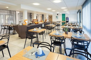 A modern dining area with multiple tables and chairs, a central counter with a coffee machine, and a view of the outdoors.