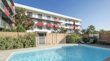 Un bâtiment moderne doté de balcons, d’une piscine et d’un espace extérieur aménagé pour s’asseoir.