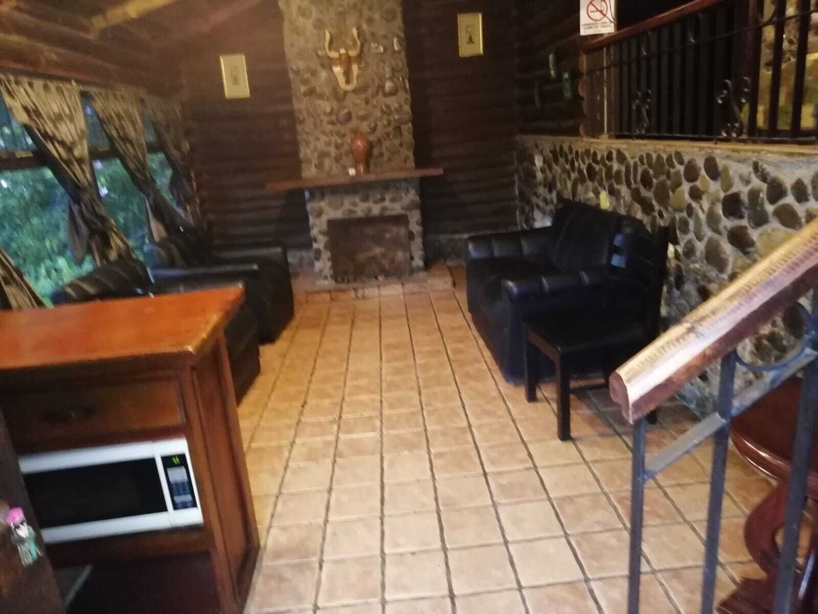 A log cabin interior with a stone fireplace, leather sofa, and a wooden table.