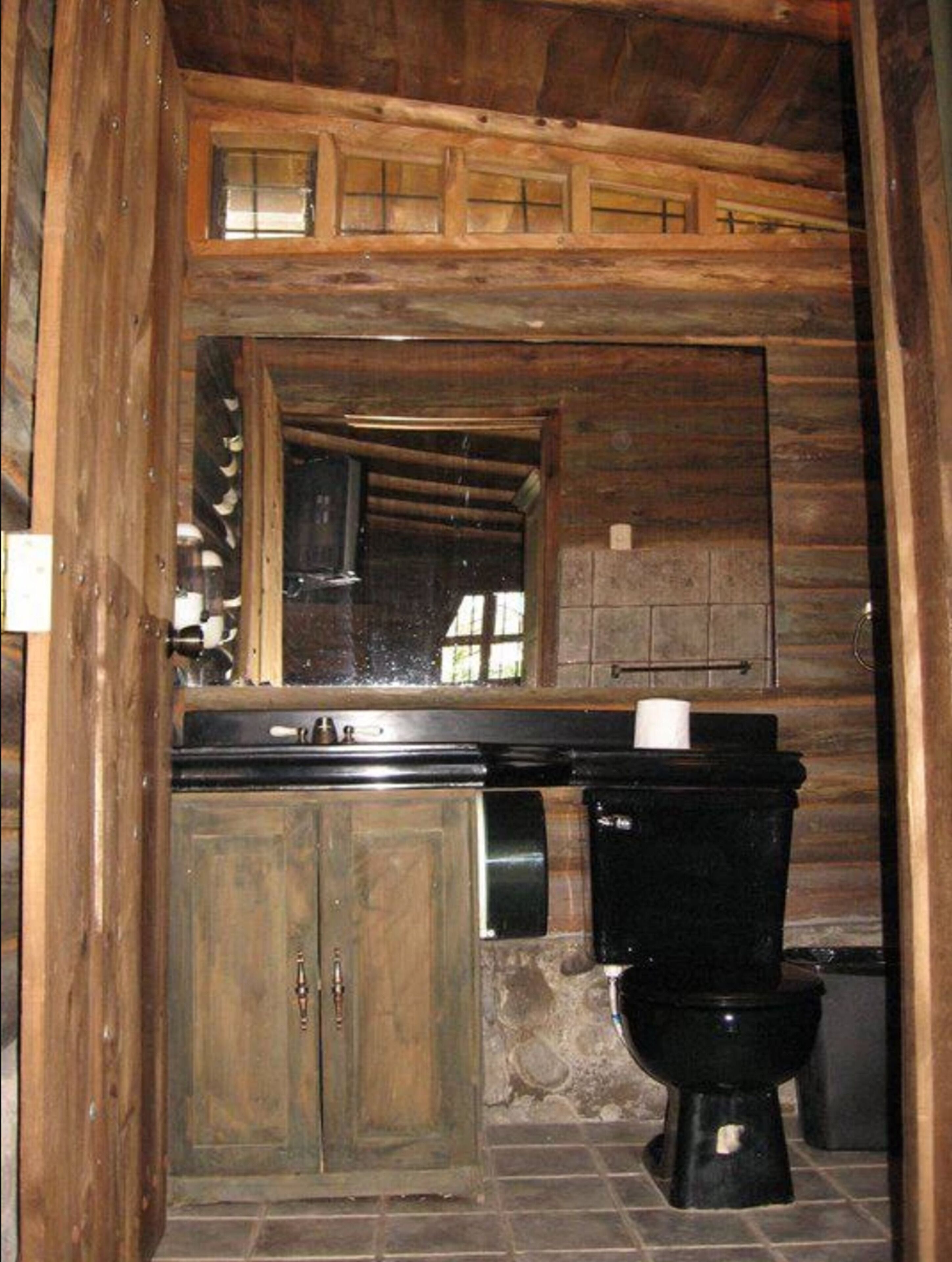 A rustic bathroom with wooden walls, a stone sink, and a black toilet.