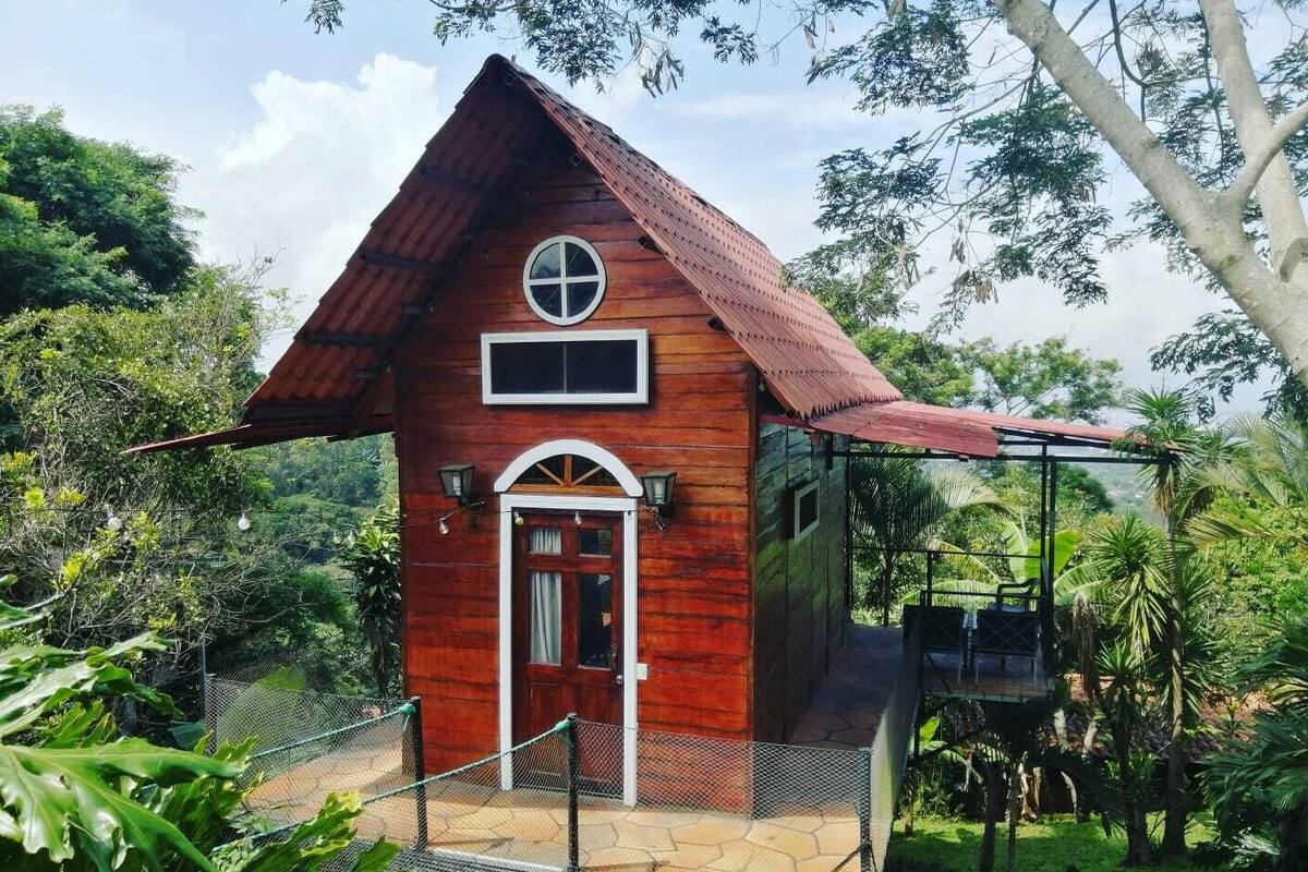 Una cabaña de madera con techo a dos aguas, un ventanal circular y un pequeño balcón.