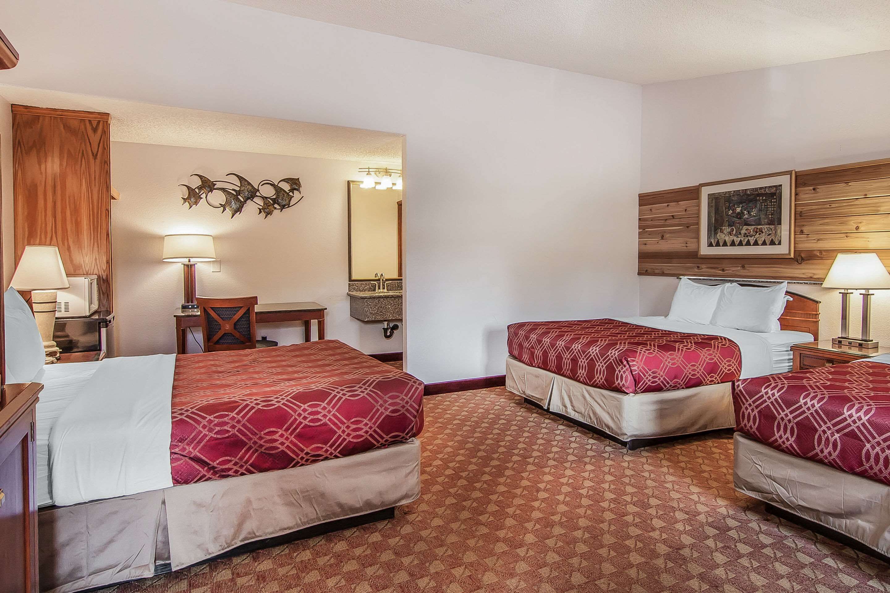A hotel room with two beds, a desk, a chair, a mirror, and a wall-mounted picture.